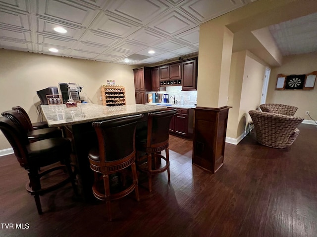 bar with light stone counters and dark wood-type flooring