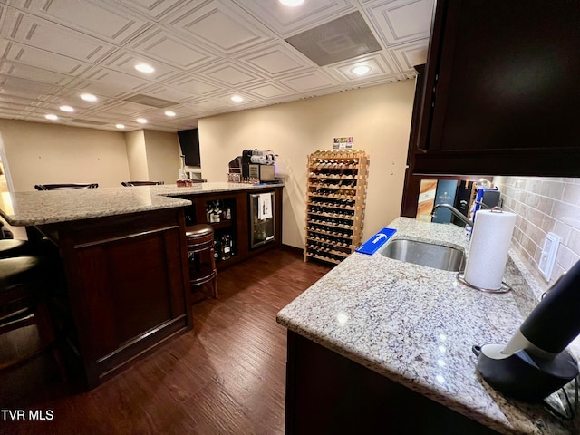 kitchen featuring dark wood-type flooring, light stone counters, dark brown cabinetry, and sink