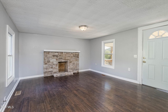 unfurnished living room featuring dark wood-type flooring, a textured ceiling, and a stone fireplace