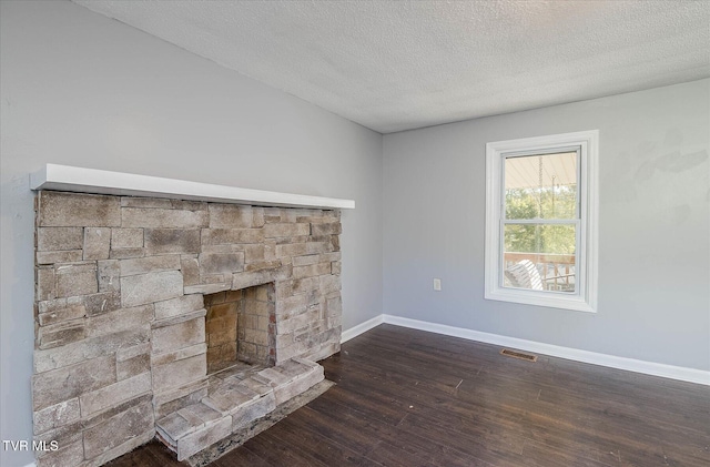 unfurnished living room with a stone fireplace, a textured ceiling, and dark wood-type flooring