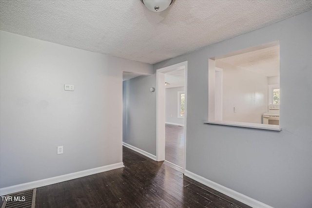 empty room with a textured ceiling, dark hardwood / wood-style flooring, and a wealth of natural light