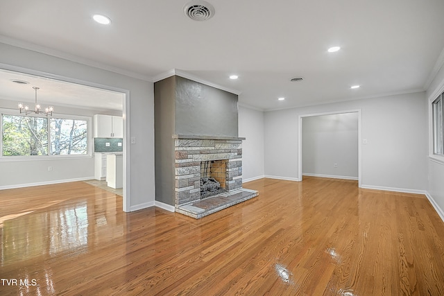 unfurnished living room with ornamental molding, light hardwood / wood-style floors, a chandelier, and a stone fireplace