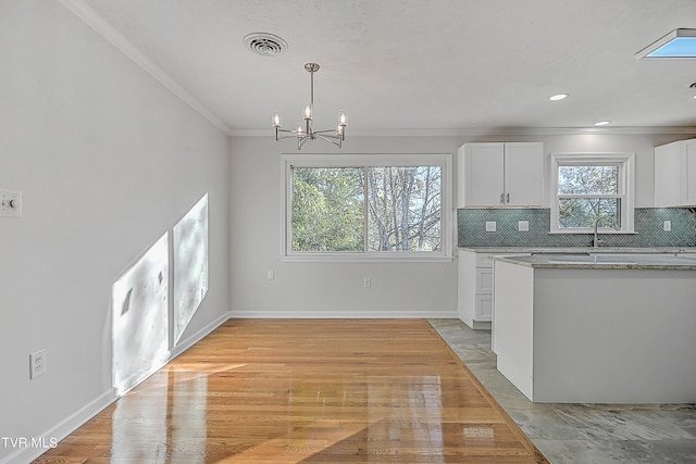 kitchen with light wood-type flooring, a healthy amount of sunlight, decorative light fixtures, and white cabinets