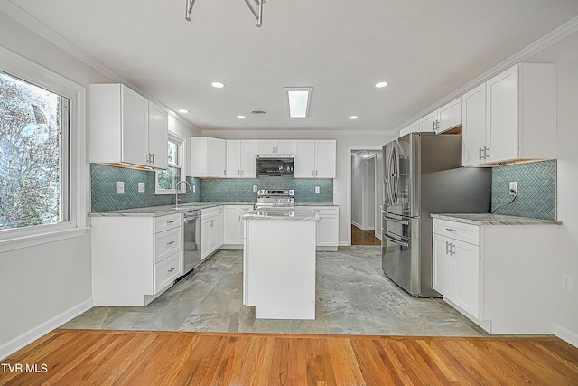 kitchen with ornamental molding, a kitchen island, white cabinetry, appliances with stainless steel finishes, and light hardwood / wood-style floors