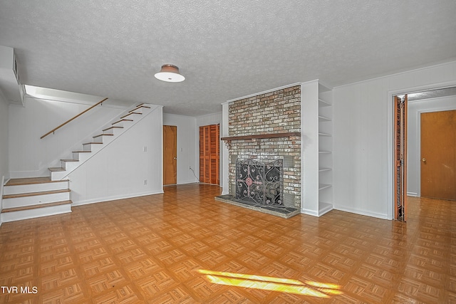 unfurnished living room featuring a brick fireplace, light parquet flooring, built in features, and a textured ceiling