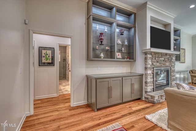 bar with a fireplace, ornamental molding, gray cabinets, and light hardwood / wood-style flooring