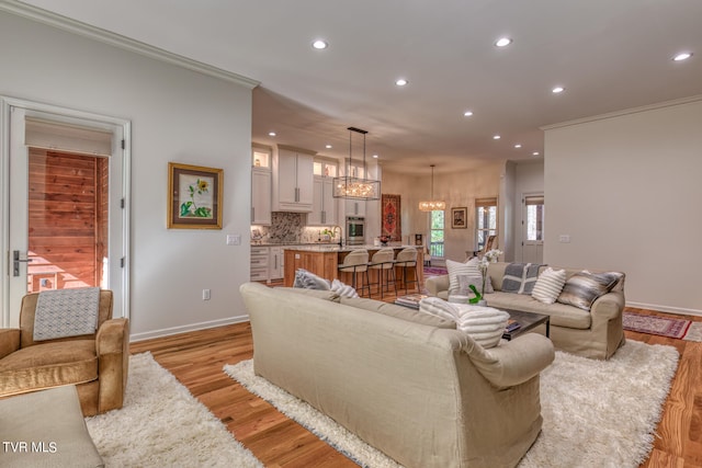 living room with a notable chandelier, crown molding, sink, and light hardwood / wood-style flooring