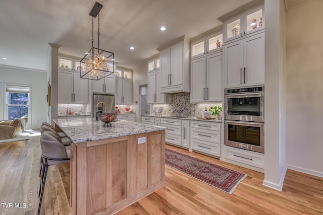 kitchen featuring a center island with sink, light stone counters, appliances with stainless steel finishes, and light hardwood / wood-style flooring