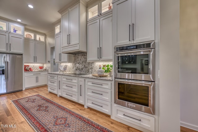 kitchen featuring light hardwood / wood-style flooring, light stone counters, backsplash, appliances with stainless steel finishes, and white cabinetry