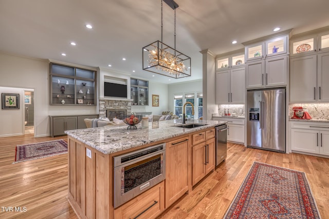 kitchen featuring a kitchen island with sink, light wood-type flooring, light stone counters, a stone fireplace, and stainless steel appliances