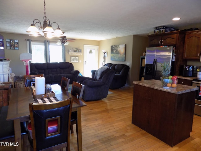 dining room with ceiling fan with notable chandelier, a textured ceiling, and light hardwood / wood-style flooring