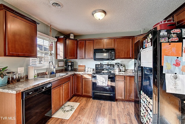 kitchen with a textured ceiling, black appliances, sink, and light hardwood / wood-style flooring