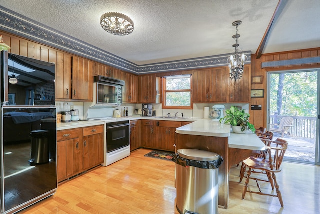 kitchen with black appliances, light hardwood / wood-style floors, kitchen peninsula, hanging light fixtures, and a textured ceiling