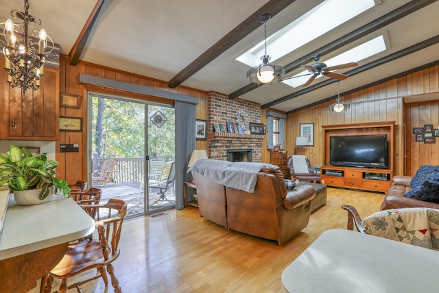 living room featuring wood walls, a brick fireplace, light wood-type flooring, ceiling fan, and lofted ceiling with skylight