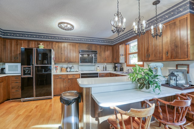 kitchen featuring pendant lighting, sink, a textured ceiling, black appliances, and light wood-type flooring