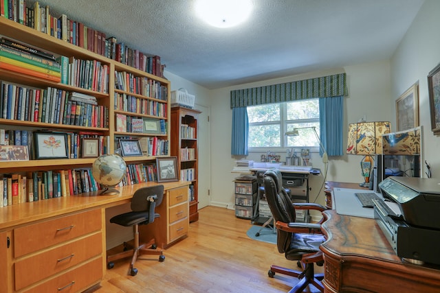 home office featuring light wood-type flooring and a textured ceiling