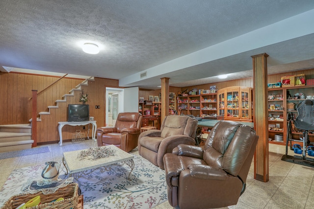 living room featuring a textured ceiling, wooden walls, and decorative columns