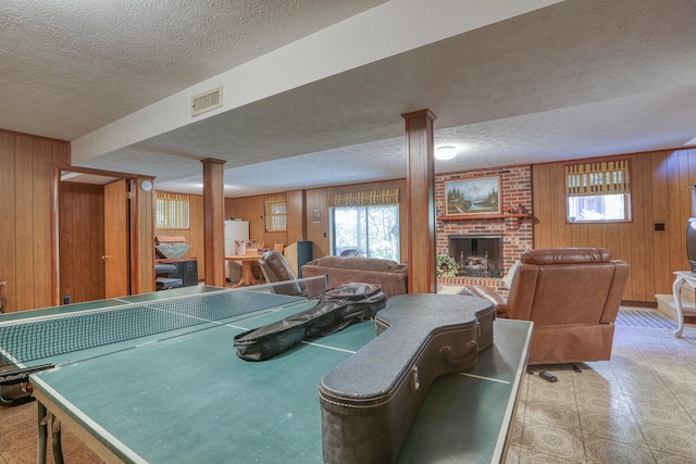 game room with ornate columns, a fireplace, wooden walls, and a textured ceiling