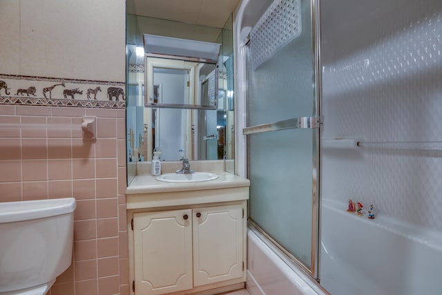 full bathroom featuring bath / shower combo with glass door, vanity, tile walls, and toilet