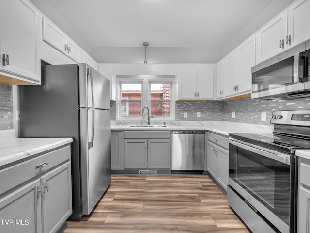 kitchen with gray cabinetry, tasteful backsplash, appliances with stainless steel finishes, sink, and light wood-type flooring
