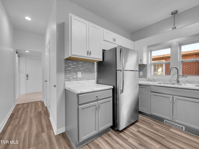 kitchen with gray cabinetry, tasteful backsplash, sink, light wood-type flooring, and stainless steel fridge
