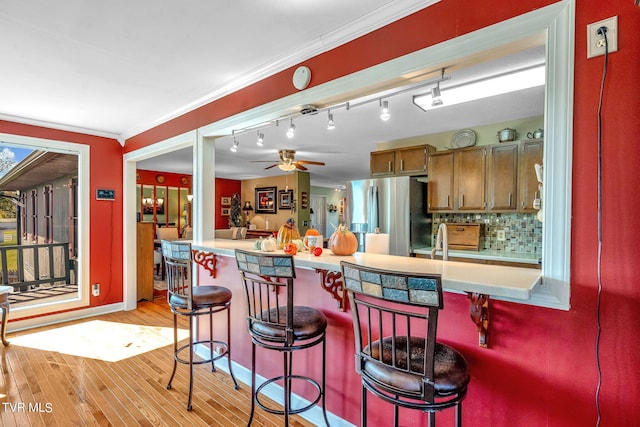 kitchen featuring tasteful backsplash, light hardwood / wood-style flooring, stainless steel fridge with ice dispenser, a breakfast bar area, and crown molding