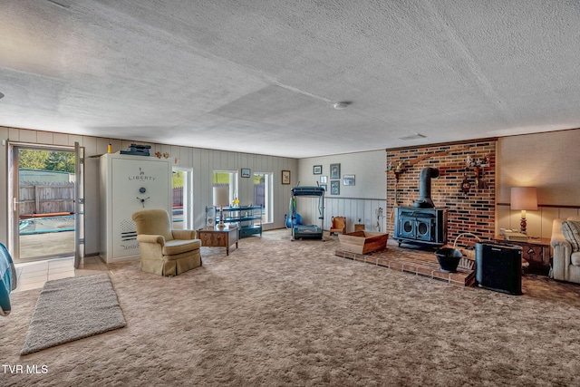 carpeted living room featuring a textured ceiling, wood walls, a wood stove, and a healthy amount of sunlight