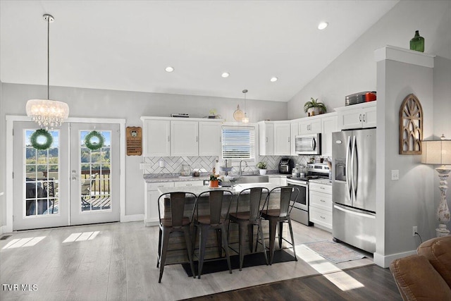 kitchen with a kitchen island, light hardwood / wood-style floors, pendant lighting, appliances with stainless steel finishes, and a kitchen bar