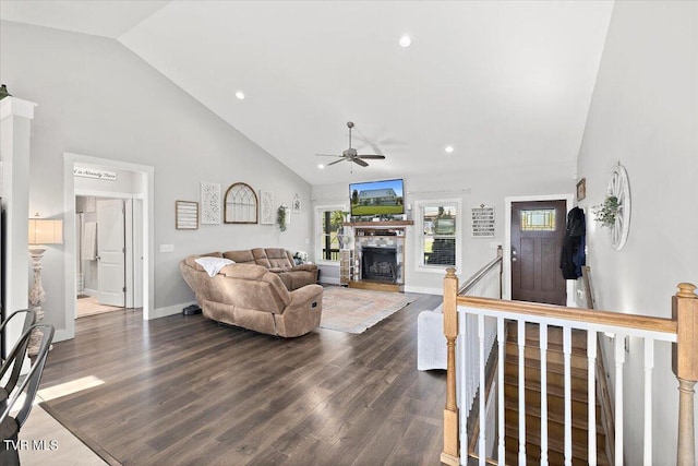 living room featuring high vaulted ceiling, ceiling fan, a stone fireplace, and dark hardwood / wood-style flooring