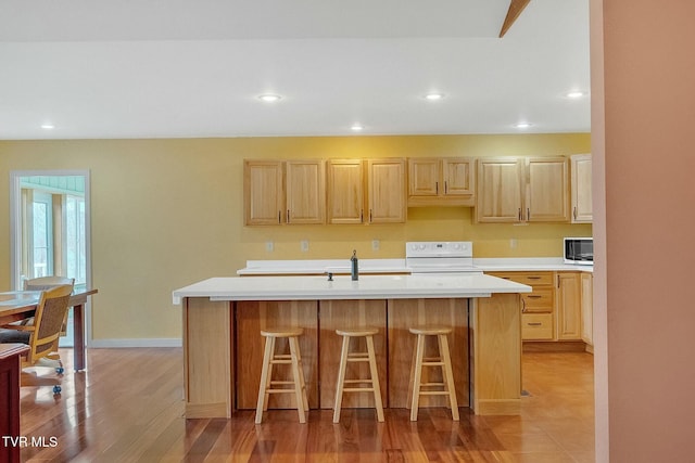 kitchen featuring stove, a breakfast bar, light brown cabinets, a center island with sink, and light hardwood / wood-style floors