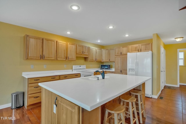 kitchen with a breakfast bar, white appliances, sink, an island with sink, and light brown cabinetry