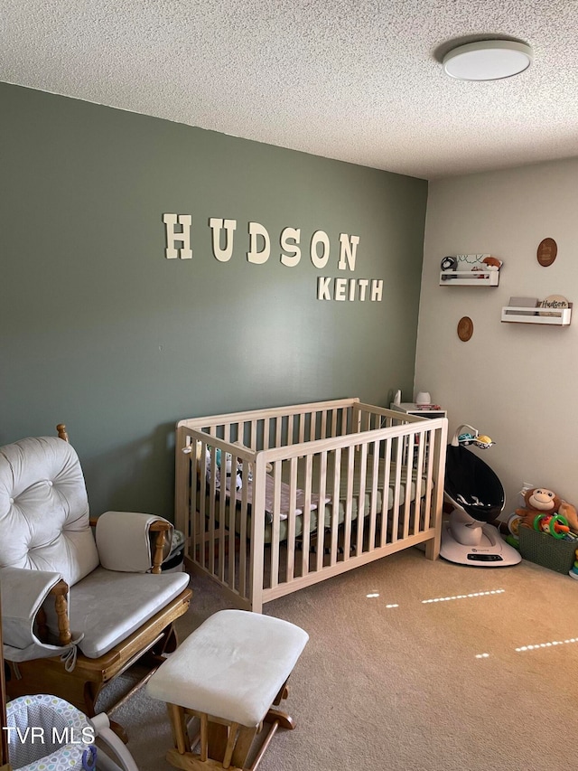 bedroom featuring carpet, a nursery area, and a textured ceiling