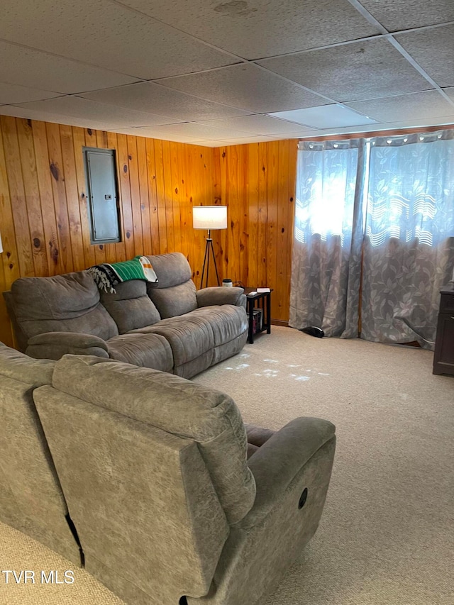 carpeted living room featuring a drop ceiling, wood walls, and electric panel