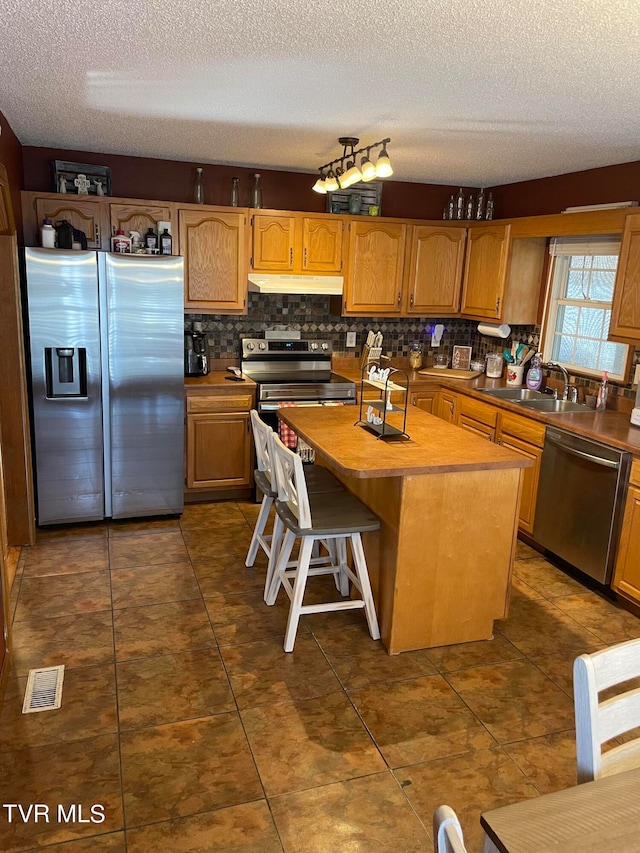 kitchen with appliances with stainless steel finishes, a textured ceiling, a kitchen island, a breakfast bar, and sink