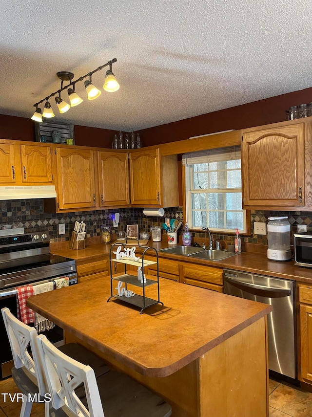 kitchen featuring a textured ceiling, appliances with stainless steel finishes, a kitchen island, sink, and light tile patterned floors