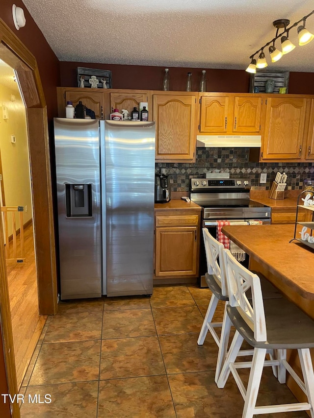 kitchen featuring decorative backsplash, dark tile patterned floors, appliances with stainless steel finishes, a textured ceiling, and track lighting