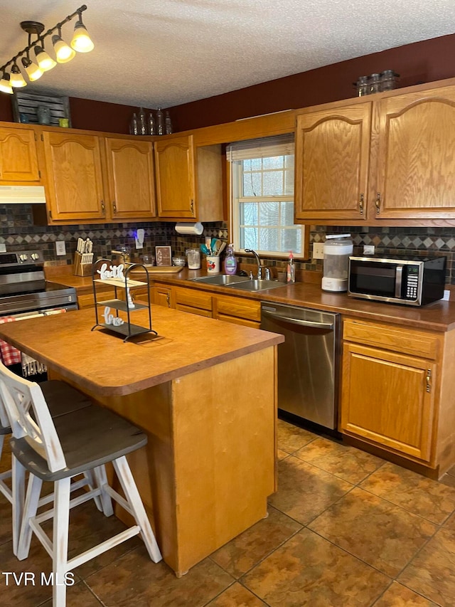 kitchen featuring a center island, a breakfast bar, sink, a textured ceiling, and stainless steel appliances