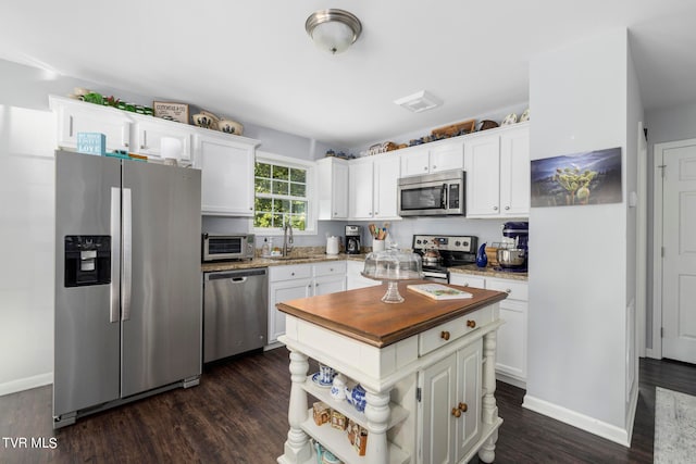 kitchen with appliances with stainless steel finishes, dark hardwood / wood-style floors, wooden counters, and white cabinetry