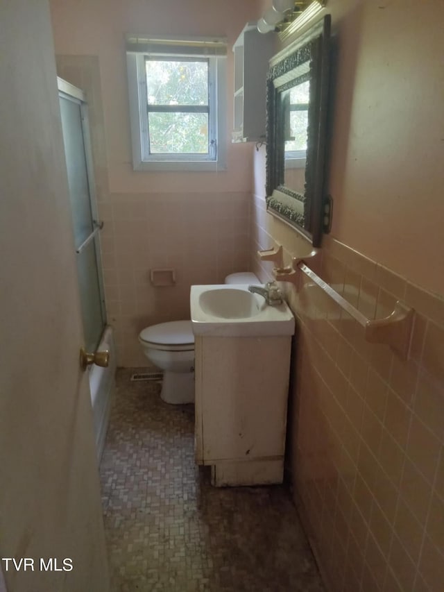 bathroom with walk in shower, vanity, tile walls, and toilet