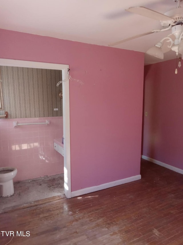 empty room featuring ceiling fan, tile walls, and wood-type flooring