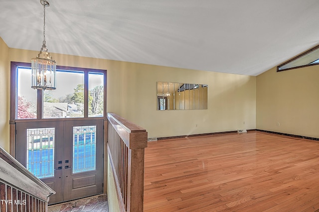 entrance foyer featuring a notable chandelier, vaulted ceiling, wood-type flooring, and french doors