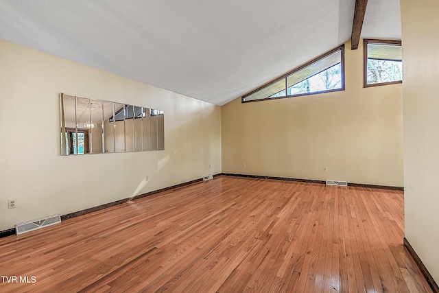 empty room with lofted ceiling with beams, light wood-type flooring, and a textured ceiling