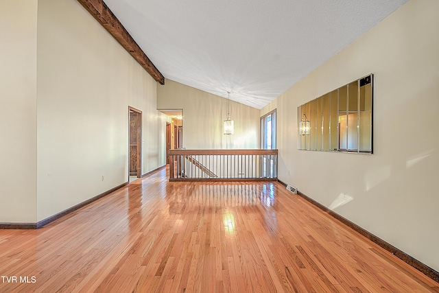 empty room featuring hardwood / wood-style floors, vaulted ceiling with beams, and a textured ceiling