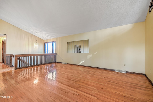 interior space with a textured ceiling, light wood-type flooring, an inviting chandelier, and vaulted ceiling