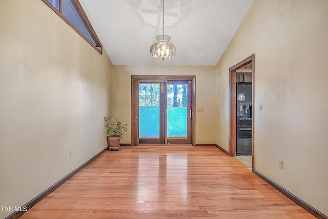 doorway with light hardwood / wood-style floors, an inviting chandelier, and vaulted ceiling