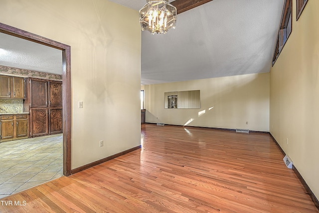 unfurnished living room with a chandelier, vaulted ceiling, a textured ceiling, and light hardwood / wood-style flooring