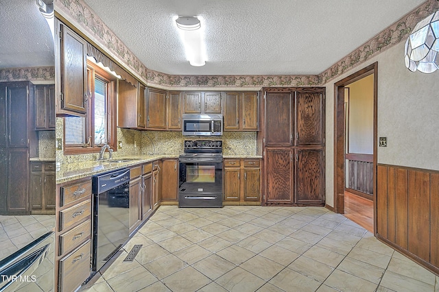 kitchen with light stone countertops, a textured ceiling, sink, black appliances, and wood walls