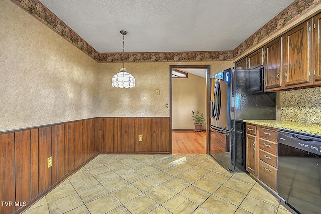 kitchen with light stone countertops, tasteful backsplash, black appliances, hanging light fixtures, and wood walls