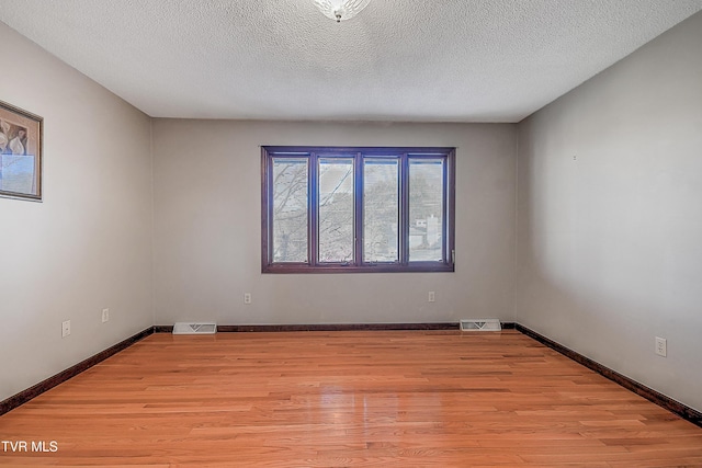 unfurnished room with light wood-type flooring and a textured ceiling