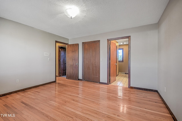 unfurnished bedroom with a textured ceiling, ensuite bathroom, and light hardwood / wood-style flooring